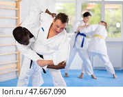 Judo or jiu-jitsu classes - two men practicing grabbing and throwing on sports mats under the guidance of trainer. Стоковое фото, фотограф Яков Филимонов / Фотобанк Лори