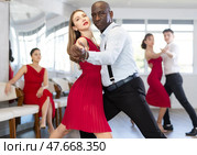 Beautiful young caucasian woman in red dress at dance salon with her African american partner dancing tango. Стоковое фото, фотограф Яков Филимонов / Фотобанк Лори