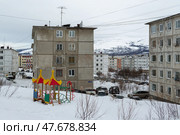 Город Магадан, Магаданская область, Россия. Вид на городской квартал и заснеженную детскую площадку во дворе. Множество серых панельных зданий. Холодная снежная погода. Повседневная жизнь в Сибири и на Дальнем Востоке России. (2018 год). Редакционное фото, фотограф Андрей Степанов / Фотобанк Лори