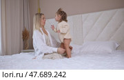 Attractive young woman and little cute girl are spending time together in bedroom at home. Mother with baby daughter dancing on bed, hugging and having fun. Happy family concept. Mother's day. Стоковое видео, видеограф Ирина Михайличенко / Фотобанк Лори