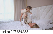 Attractive young woman and little cute girl are spending time together in bedroom at home. Smiling mom lying on bed hold excited small girl child on legs up in air. Happy family concept. Mother's day. Стоковое видео, видеограф Ирина Михайличенко / Фотобанк Лори