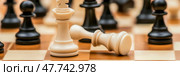 Triumph and Defeat: A white king stands as another white piece lays fallen amid dark pawns, a scene of strategic battle. Стоковое AI-изображение, AI-художник Данила Большаков / Фотобанк Лори