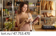 Young girl using smartphone to scan package of cured sausage for detailed product information while shopping in grocery store. Concept of modern technology assisting consumers. Стоковое видео, видеограф Яков Филимонов / Фотобанк Лори