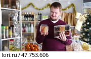 Man holds a set of dried fruit next to the shelves of food in a Christmas supermarket. Buyer chooses sweet desserts for the New Year's dinner and holiday. Стоковое видео, видеограф Яков Филимонов / Фотобанк Лори