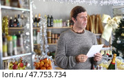 Portrait of modern man with cart shopping at supermarket, looking for something and reviewing and checking list of products to buy. Christmas shopping. Стоковое видео, видеограф Яков Филимонов / Фотобанк Лори