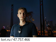 A man stands tall in a dark environment, showcasing a confident demeanor. The backdrop features the impressive Dubai skyline illuminated by city lights. Стоковое фото, фотограф Aleksandr Golubev / Фотобанк Лори