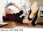 Relaxed elderly female office employee playing games on smartphone. Стоковое фото, фотограф Яков Филимонов / Фотобанк Лори