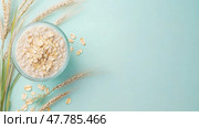 Oats and wheat arranged aesthetically on a light blue background with fresh grains beside a glass bowl of oatmeal. Стоковое AI-изображение, AI-художник Сергей Толмачёв / Фотобанк Лори
