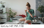 Young woman drinking coffee, taking study break in cozy room. Surrounded by open notebooks, markers, and headphones, she enjoys moment of relaxation before resuming learning. Стоковое видео, видеограф Енваев Андрей / Фотобанк Лори