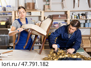 Professional male and female artisans restorers in uniform renovating antique chair mirror frame while working in repair shop. Стоковое фото, фотограф Яков Филимонов / Фотобанк Лори