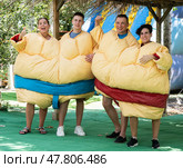 Cheerful friends posing in inflatable sumo twin suits in outdoor amusement park. Стоковое фото, фотограф Яков Филимонов / Фотобанк Лори