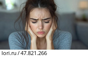 A young woman sits in a gentle light, visibly stressed, with her hands on her head, conveying a moment of overwhelming emotions in a cozy space. Стоковое AI-изображение, AI-художник Данила Большаков / Фотобанк Лори
