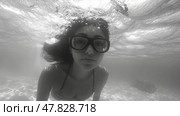 A young woman dives beneath the water's surface, showcasing her goggles and flowing hair in a calm underwater setting illuminated by light. Стоковое AI-изображение, AI-художник Данила Большаков / Фотобанк Лори