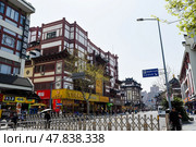 Shanghai, China - 1 April 2025: City street in Shanghai with traditional Chinese architecture, shops and pedestrians. Sunny day with carved decorations and red accents on buildings. Редакционное фото, фотограф Татьяна Терехина / Фотобанк Лори