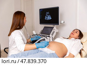 The pregnant woman is lying down in a hospital, doctor using ultrasound equipment screening of pregnant woman. Patient at ultrasonography examination. Family planning and IVF centers concept. Стоковое фото, фотограф Ирина Михайличенко / Фотобанк Лори