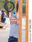 Lifestyle. A cute little boy is hanging on rings on a sports field in the fresh air. The concept of children's sports and physical development. Стоковое фото, фотограф Photojuli / Фотобанк Лори