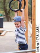 Lifestyle. A cute little boy is hanging on rings on a sports field in the fresh air. The concept of children's sports and physical development. Стоковое фото, фотограф Photojuli / Фотобанк Лори