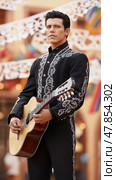 Cinco de Mayo mariachi musician with guitar in traditional suit and festive papel picado. Стоковое AI-изображение, AI-художник Анастасия Золотницкая / Фотобанк Лори