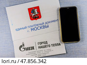Оплата услуг ЖКХ онлайн. Единый платёжный документ ЕПД, документ на оплату от МОЭК, смартфон с интернетом лежат на столе. Удобно, быстро, не выходя из дома. Москва. Редакционное фото, фотограф Владимир Устенко / Фотобанк Лори
