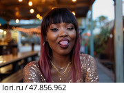 A woman with striking hair color expresses joy by playfully sticking out her tongue at an outdoor gathering as evening sets in. Стоковое AI-изображение, AI-художник Данила Большаков / Фотобанк Лори