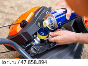 Filling a petrol lawn mower with motor oil to lubricate the engine. Preparing the lawn mower for operation. Стоковое фото, фотограф Коханова Наталья / Фотобанк Лори