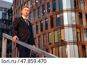 A businessman stands on a staircase, gazing thoughtfully into the distance. The contemporary architecture reflects the warm glow of the evening sun, creating an inspiring atmosphere for ambition. Стоковое фото, фотограф Aleksandr Golubev / Фотобанк Лори