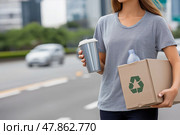 A Girl in plain colors T-shirt carries a box of recyclables. Стоковое AI-изображение, AI-художник Ирина Ручушкина / Фотобанк Лори