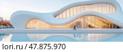 Modern architectural wonder: Man walking by a sinuous building with glass facade and reflections. Стоковое AI-изображение, AI-художник Данила Большаков / Фотобанк Лори