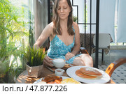 Summer breakfast on the bright veranda. A smiling European woman in a light green summer dress drinks cappuccino coffee at a wooden table. Стоковое фото, фотограф Владимир Разгуляев / Фотобанк Лори
