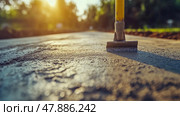 A construction worker uses a screed tool to level a fresh layer of concrete on a pathway as the sun sets, casting a warm glow over the area. Стоковое AI-изображение, AI-художник Данила Большаков / Фотобанк Лори