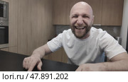 Bald man in white T-shirt sitting at table and laughing contagiously. Hysterical laughter of handsome guy. Portrait of joyful man. Стоковое видео, видеограф Ирина / Фотобанк Лори