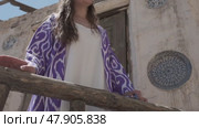 A young woman with long hair in an oriental robe and skullcap stands in the wind near an ancient mosque. Стоковое видео, видеограф Aleksey Kidisyuk / Фотобанк Лори