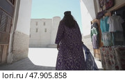 A young woman with long hair in an oriental robe and a skullcap walks through an ancient oriental city. Стоковое видео, видеограф Aleksey Kidisyuk / Фотобанк Лори