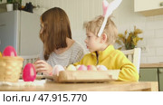 Children siblings painting Easter egg sitting together at table. Easter Family traditions. Teen girl teaching happy little brother and sister to dye, decorate eggs with paints. Preparation to holidays. Стоковое видео, видеограф Марина Демидюк / Фотобанк Лори