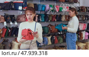 Woman stopped near accessories showcase, holds lady handbag in hands and examines product. Стоковое видео, видеограф Яков Филимонов / Фотобанк Лори