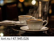 Espresso cups. Side view two small cups filled of rich coffee. Freshly brewed coffee shots. Black table. Cafe settings background, caffeine. Spoons, saucers. Refreshing hot cup of strong coffee. Стоковое AI-изображение, AI-художник Марина Демидюк / Фотобанк Лори