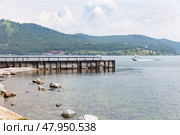 Coast of Baikal Lake on summer day. View of wooden pier in village of Port Baikal on shore of  lake. In distance beyond Angara River, village of Listvyanka is visible. Beautiful landscape. Nature background. Стоковое фото, фотограф Виктория Катьянова / Фотобанк Лори