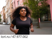 Determined overweight woman in a sleek black shirt sprints down an urban street, her movement exuding power and liberation. Стоковое AI-изображение, AI-художник Данила Большаков / Фотобанк Лори