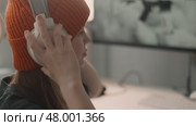 Teen girl gamer sits an ergonomic desk near monitor, puts on white headphones with microphone. Concept of smart gadgets boosting productivity, learning, and competitive gaming at home. Стоковое видео, видеограф Енваев Андрей / Фотобанк Лори