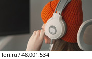 Relaxed gaming session in bright room with teen girl wearing warm beanie and headset. Modern entertainment space with keyboard, controller, and virtual reality equipment. Стоковое видео, видеограф Енваев Андрей / Фотобанк Лори