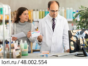 Experienced pharmacist helps girl buy medicine - he reads the prescription and compares it with data on computer. Стоковое фото, фотограф Яков Филимонов / Фотобанк Лори