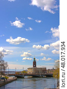 Стокгольмская ратуша (Stadshuset), вид с набережной вдоль Норрстрема, через мост Васаброн. Башня с коронами зданий возвышается на фоне озера Меларен и голубого неба с пушистыми облаками. Это один из самых знаковых видов столицы Швеции. Редакционное фото, фотограф Анна Чижова / Фотобанк Лори