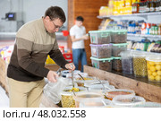 Man chooses marinated olives in supermarket, scooping them from bucket with ladle into plastic bag. Стоковое фото, фотограф Яков Филимонов / Фотобанк Лори