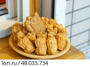 Tokyo, Japan - Sep 30 2024, A close-up view of a bowl filled with Taiyaki pies in the form of a Maneki Neko, in the window of a cafe, Tokyo, Japan. Редакционное фото, фотограф Сергей Богомяко / Фотобанк Лори