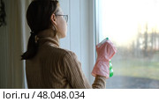 Teen girl is cleaning window in apartment. Teenager female cleaner using a squeegee to wash a window. Girl wiping, washing glasses with with spray bottle, rag and vacoom. Everyday chores. Purification. Стоковое видео, видеограф Марина Демидюк / Фотобанк Лори