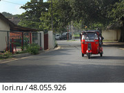 Красный тук-тук едет по тихой улице днем ​​в Галле, Шри-Ланка.  Red Tuk-Tuk Driving Down Quiet Street in Daylight in Galle, Sri Lanka (2018 год). Стоковое фото, фотограф Соболева Наталия / Фотобанк Лори