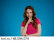 Woman posing with a shushing gesture in a studio against a bright blue background evoking a sense of curiosity and intrigue. Стоковое фото, фотограф Гурьянов Андрей / Фотобанк Лори