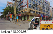 Guangzhou, China - July 12, 2024: A lively urban street scene that features parked cars alongside diverse shops and storefronts. Редакционное фото, фотограф David Kashakhi / Фотобанк Лори