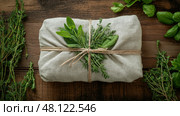 Freshly wrapped herbs tied with natural twine on a rustic wooden table. Пучок свежих трав, включая шалфей и тимьян, завернут в натуральную ткань и перевязан шпагатом. Вокруг пучка на деревянном столе разложена зелень. Стоковое AI-изображение, AI-художник Katsiaryna Repich / Фотобанк Лори
