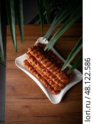 Top view of grilled chicken kebab skewers served on a white plate. The setting includes a natural wooden surface and green leaves framing the dish. Стоковое фото, фотограф Aleksandr Gavrilychev / Фотобанк Лори